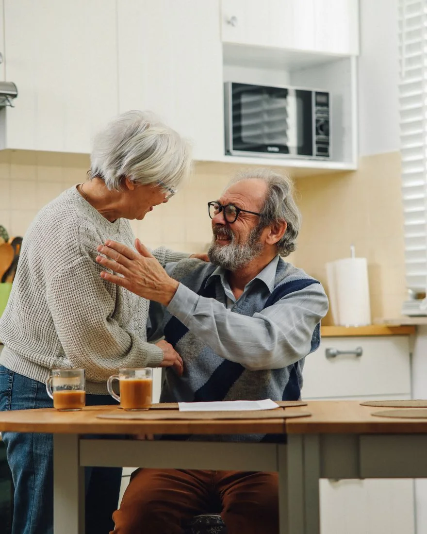Senior couple smiling and embracing in a cozy kitchen setting.