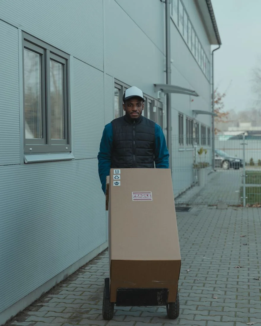 Courier delivering a package on a trolley outside a modern industrial building.
