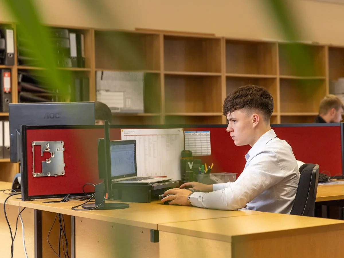 A focused young man typing on a computer in a contemporary office environment.
