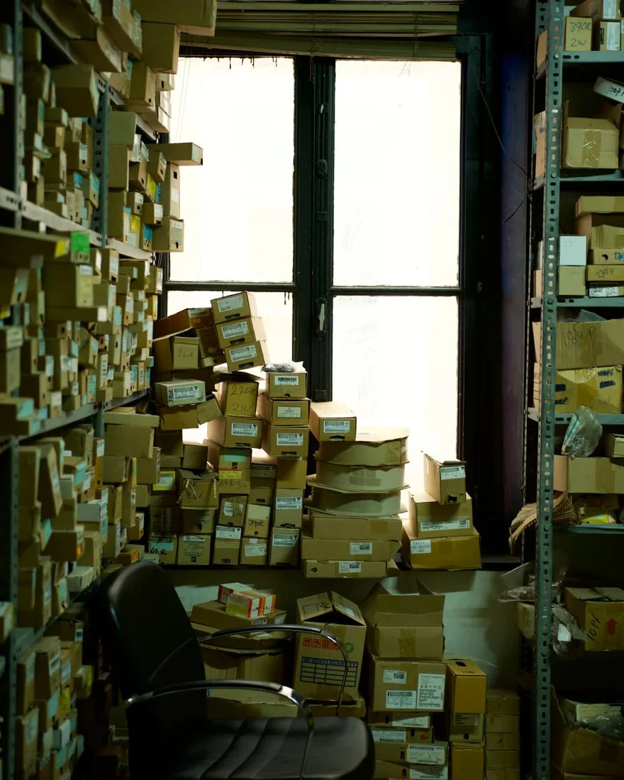 A cluttered storage room filled with cardboard boxes and an office chair by a window.