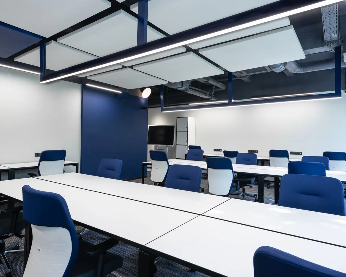 Interior of modern spacious workspace with long white tables and blue armchairs placed near monitor with black screen in business center