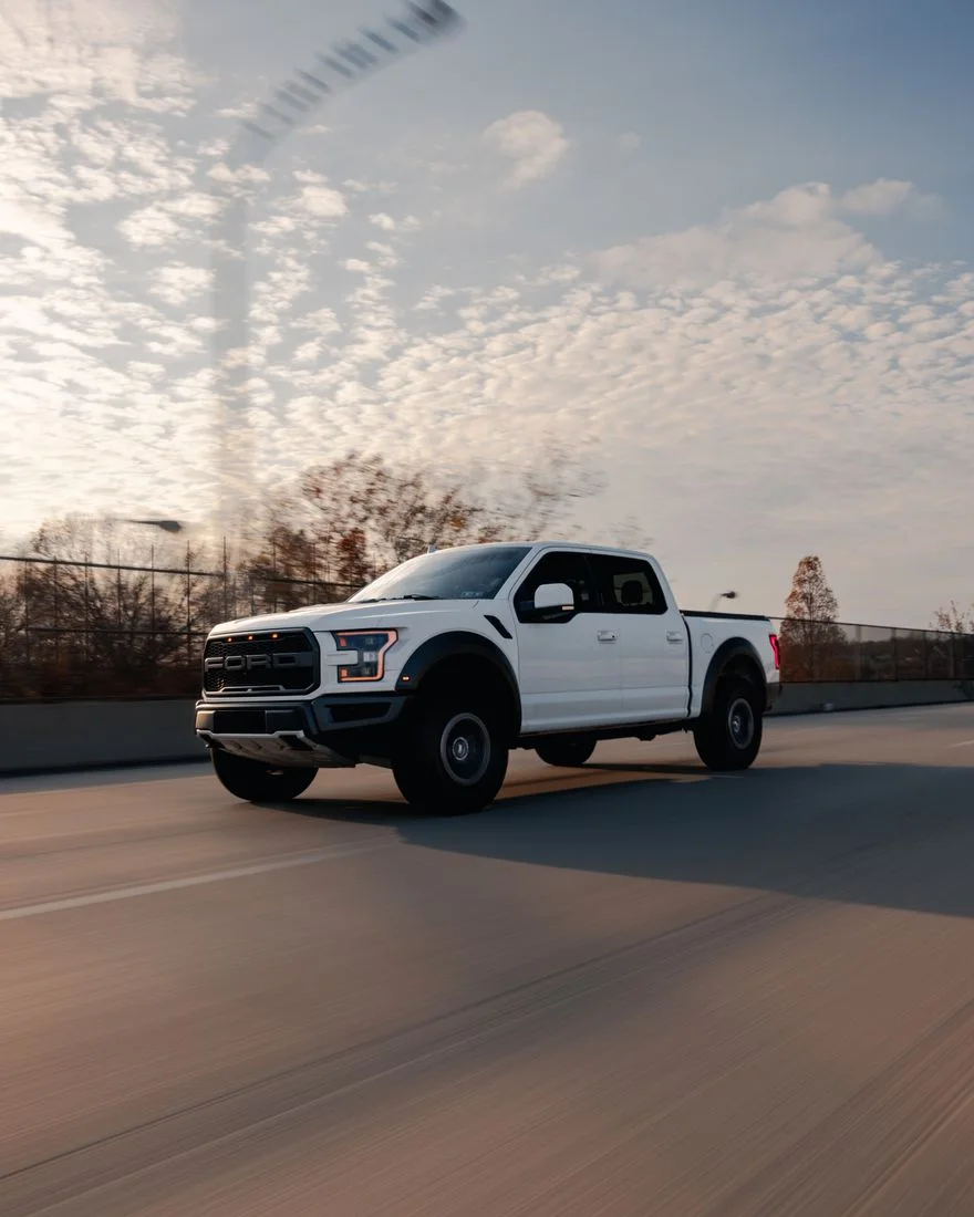 A white pickup truck speeding along a highway under a cloudy sky.