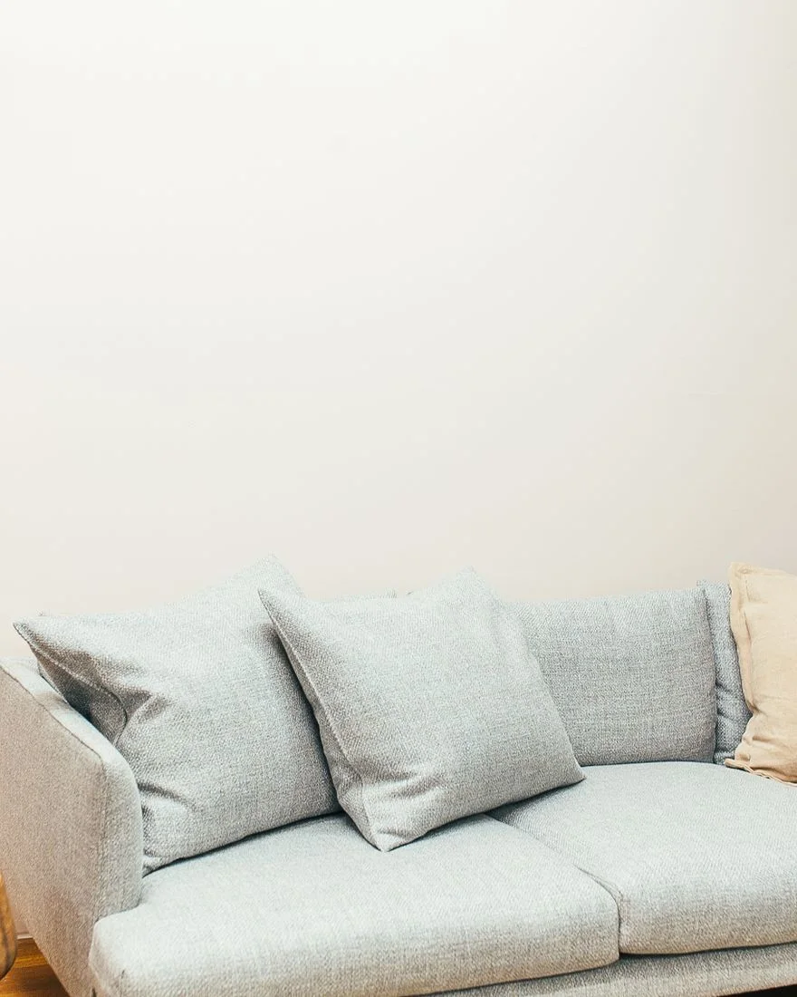 Soft couch with pillows placed in light living room on wooden floor near white wall