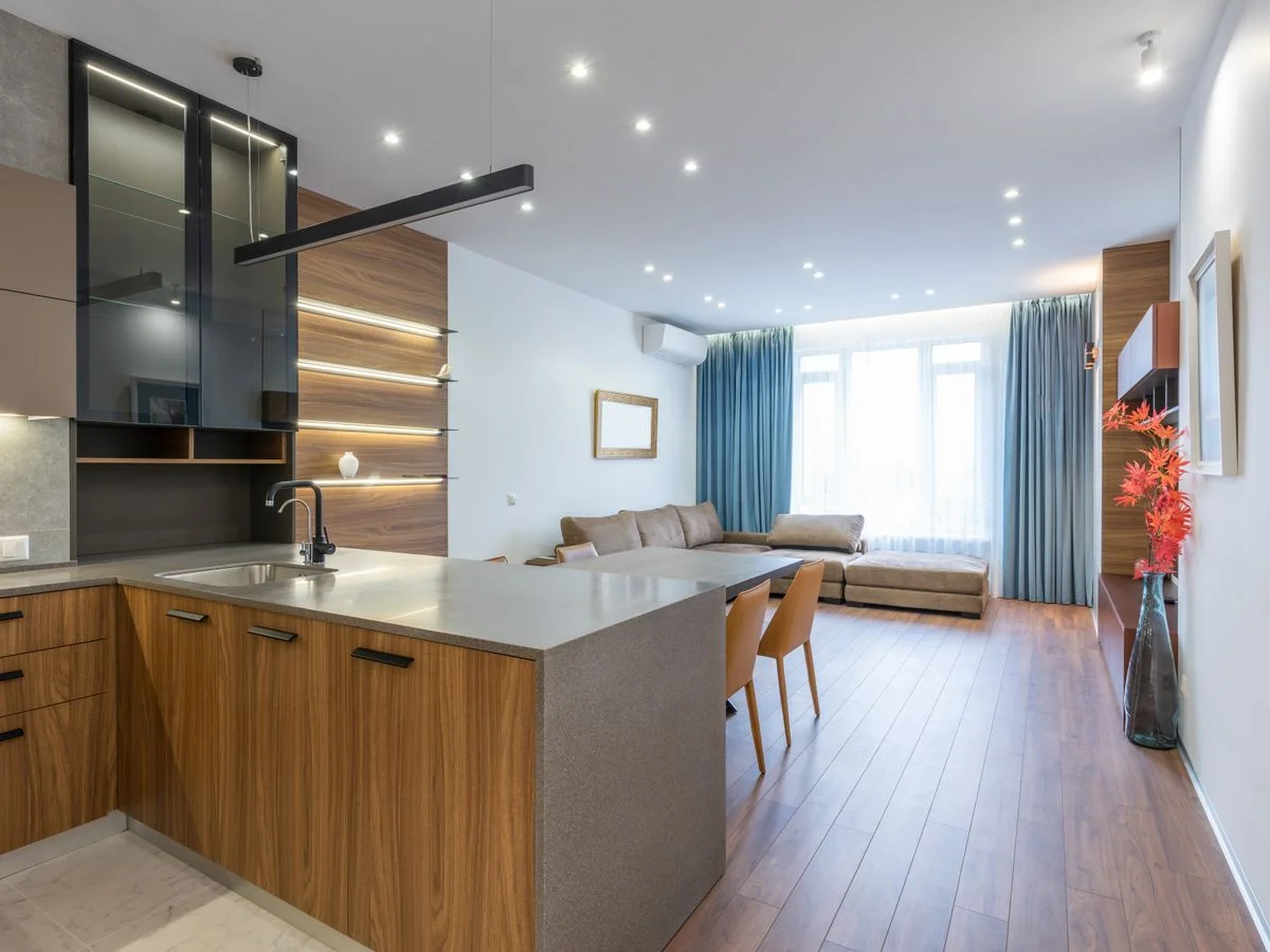 Interior of spacious flat with wooden cabinets in modern kitchen placed near table and comfortable couch near window at home