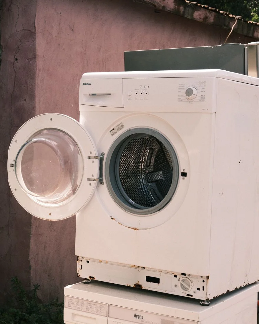 Outdoor view of two stacked laundry machines with an open door, showing rustic surroundings.