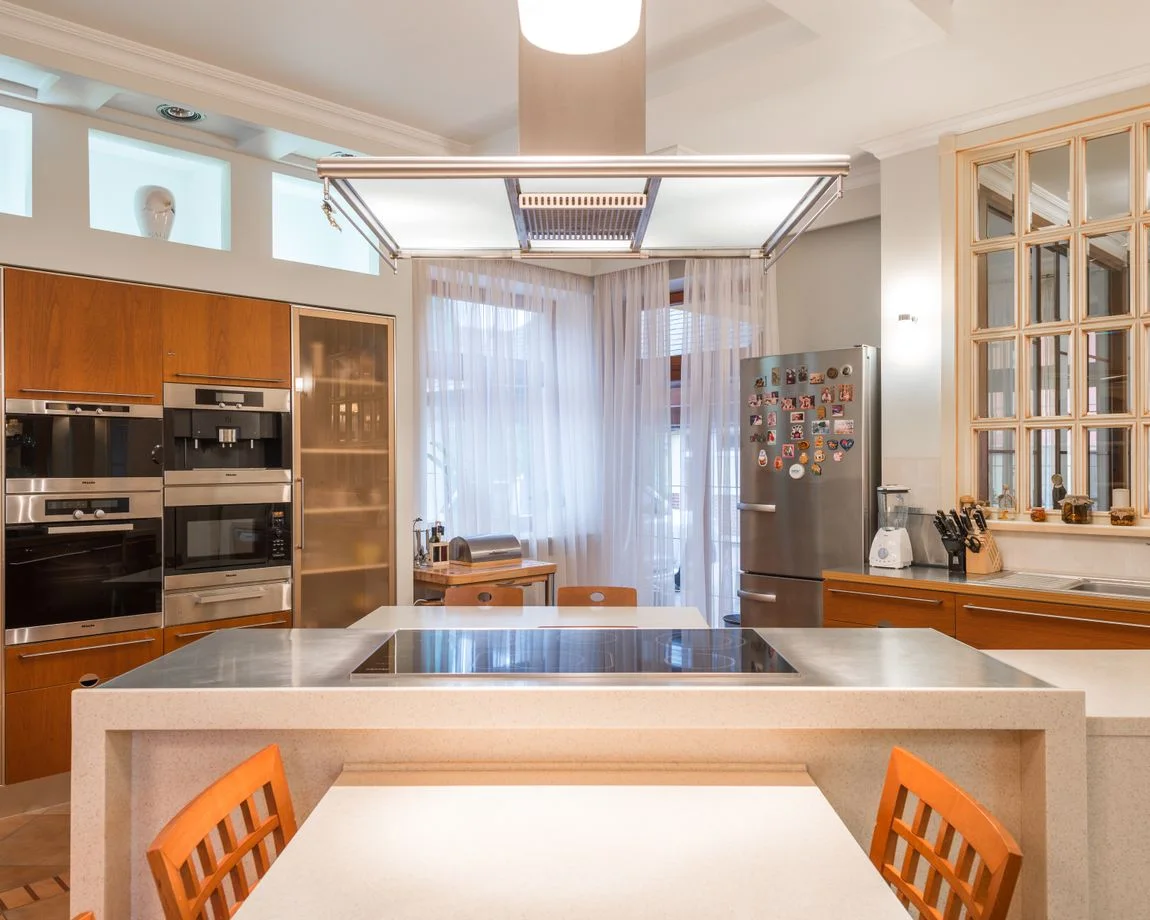 Interior of contemporary kitchen with wooden cabinets and built in appliances and island counter with stove top illuminated with bright lamps