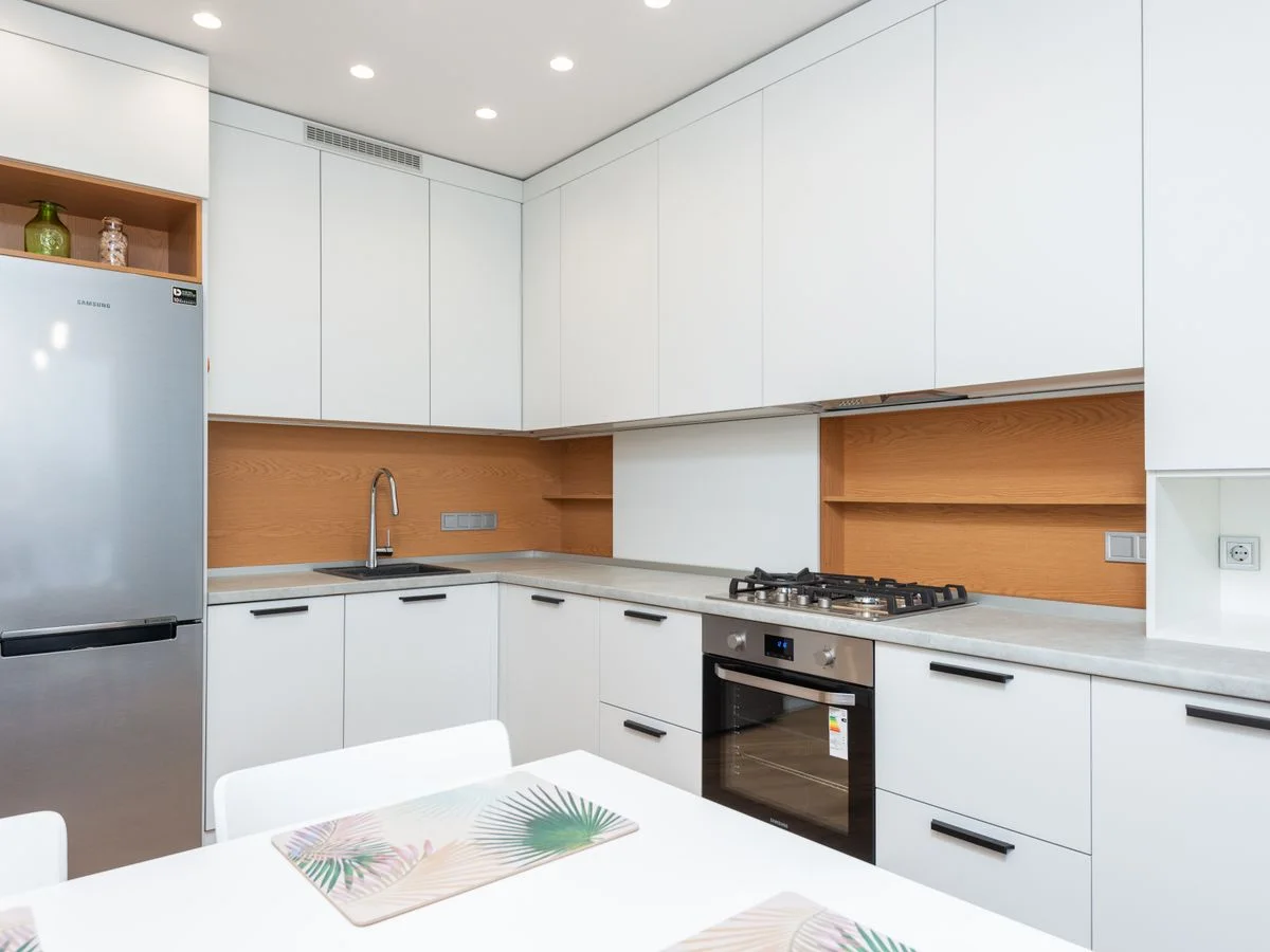 Contemporary kitchen with gas stove and oven against table with placemats and refrigerator reflecting shiny lamps in house