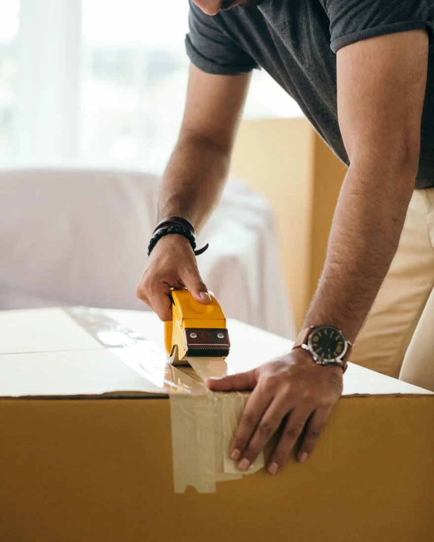 Side view of concentrated crop ethnic male sticking cardboard box with tape during preparing for moving in house at daytime