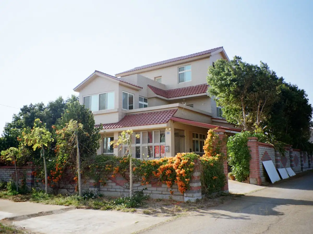 A charming suburban house with a red roof, surrounded by lush greenery and a garden, basking in daylight.