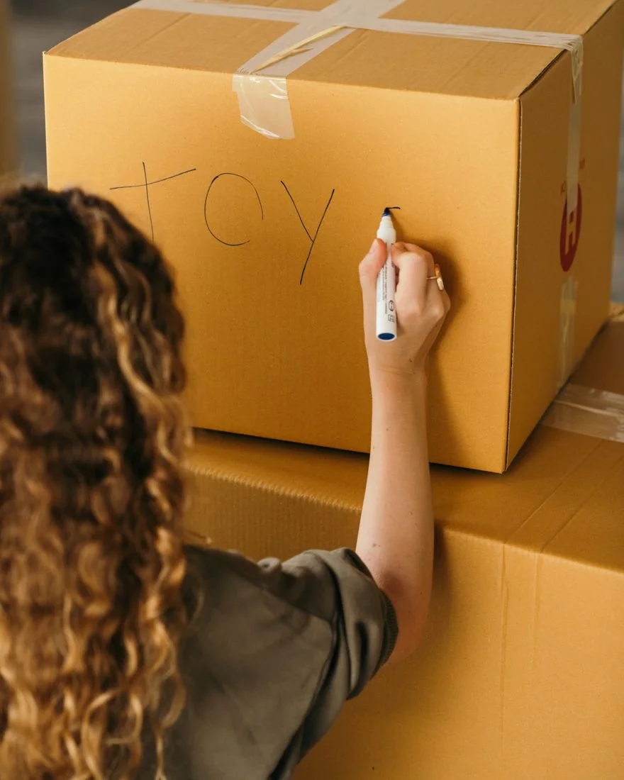 Back view of crop faceless female in casual wear labeling packed cardboard box with marker while moving house