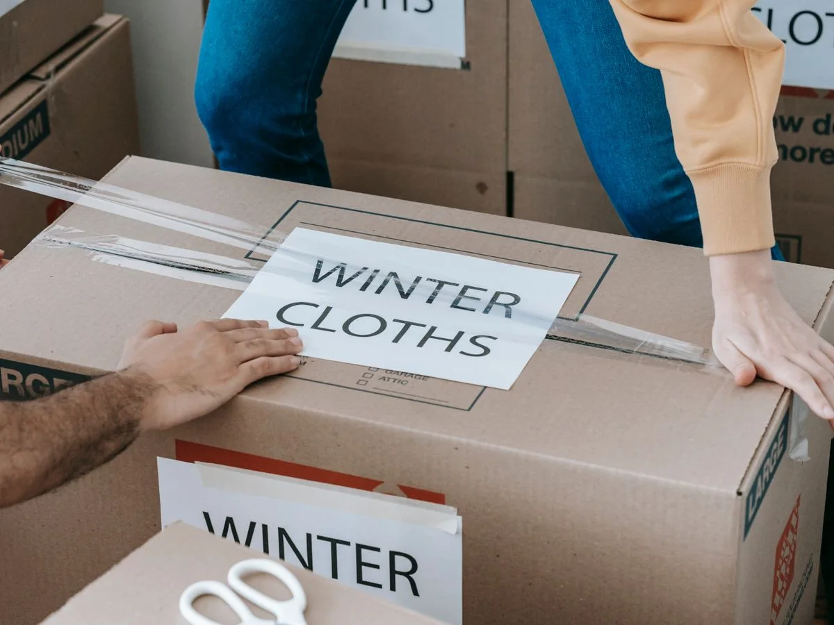 Close-up of hands packing a box labeled 'Winter Clothes' for relocation, emphasizing organized moving.