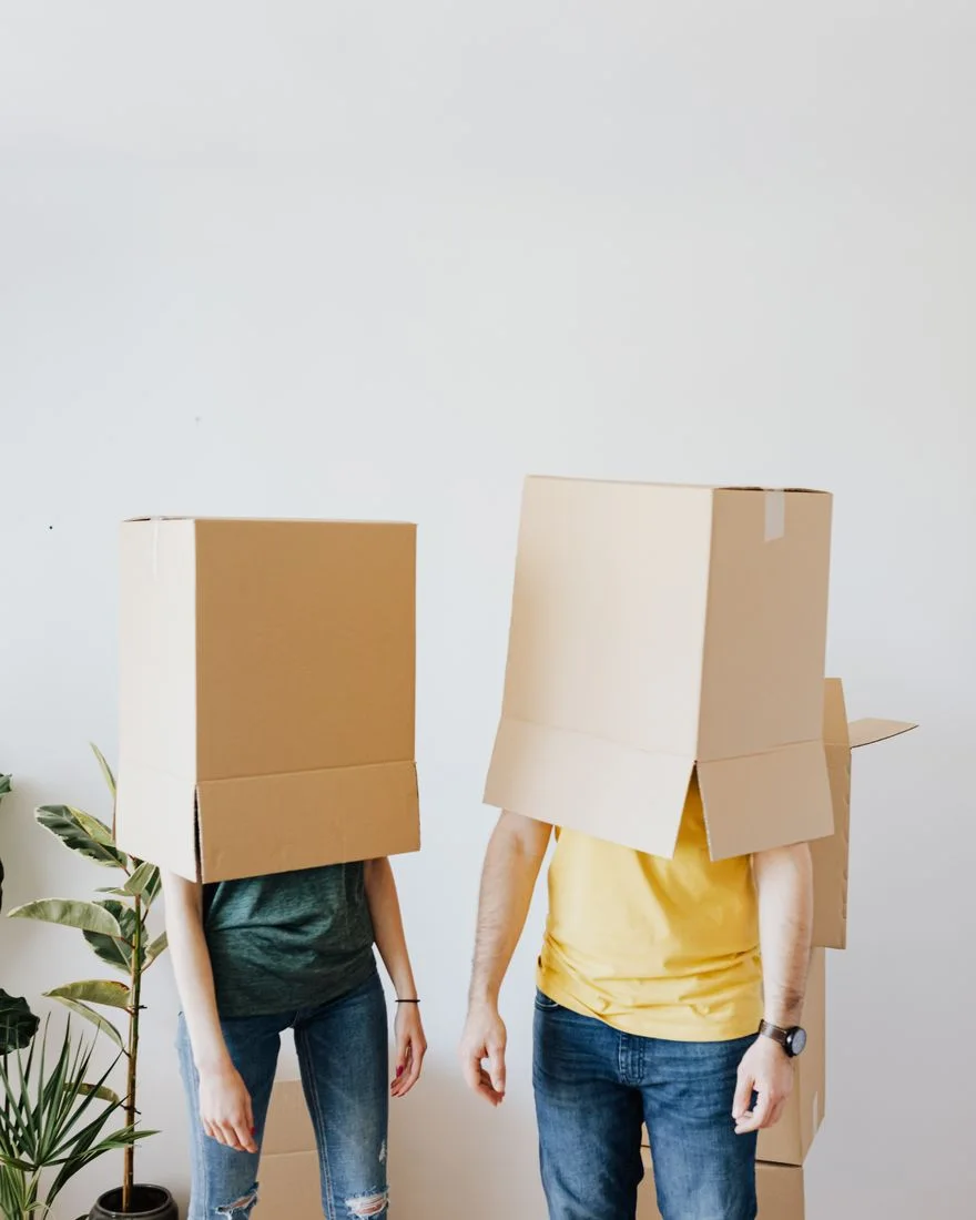 Anonymous couple in casual outfit having fun and carrying empty carton boxes on head while preparing for relocation