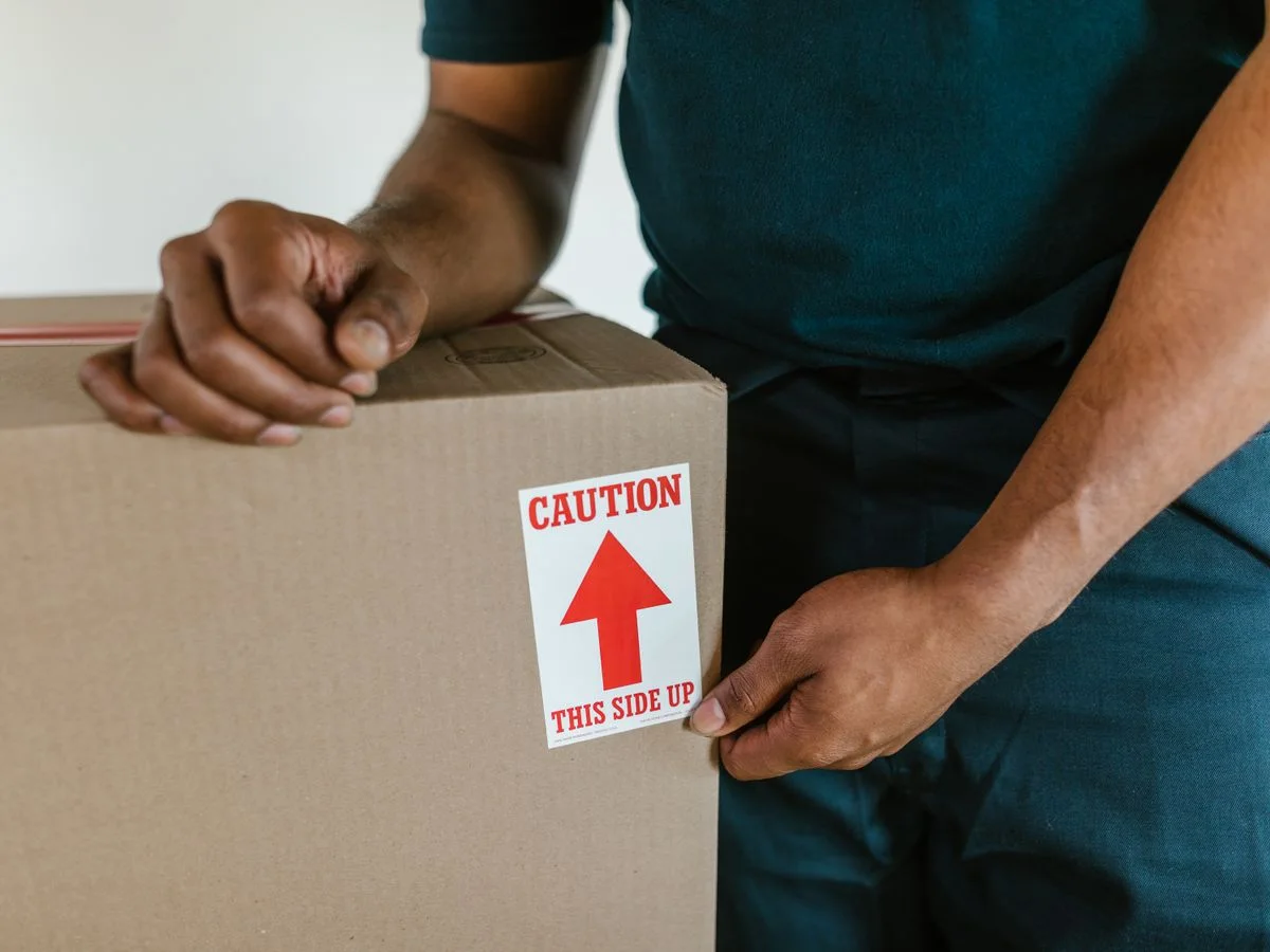 A person handling a moving box with a 'caution this side up' label indoors.